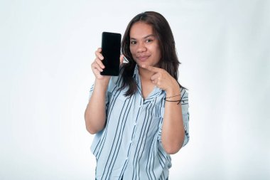 Endonezyalı mavi çizgili tişörtlü kadın elinde akıllı bir telefonla işaret parmağını boş ekrana doğrultuyor. Beyaz arkaplanda izole.