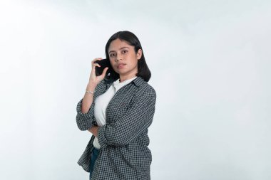 Endonezyalı genç bir kadının portresi, kısa siyah saçlı, kareli fanila gömlekli, kulağına akıllı telefon dayamış, sanki konuşuyormuş gibi. Beyaz arkaplanda izole.