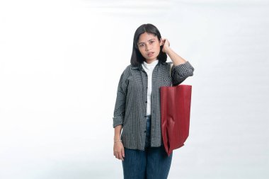 Flanel gömlekli Endonezyalı kadın saçına dokunurken kırmızı bir çanta taşıyor. Perakende alışveriş, tüketici yaşam tarzı ve beyaz arka planda izole edilmiş günlük moda kavramı.