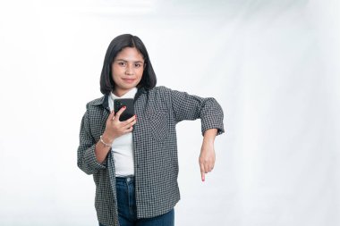 Flanel gömlekli genç Endonezyalı kadın cep telefonu tutuyor ve fotokopi alanını işaret ediyor. Beyaz arka planda mobil uygulama reklamcılığı ve dijital eğitim kavramı.