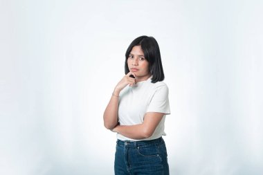 Beyaz gömlek ve kot pantolon giymiş, stüdyoda poz veren düşünceli bir Endonezyalı kadının portresi. Beyaz arka planda karar verme, düşünme ve sorun çözme kavramı.