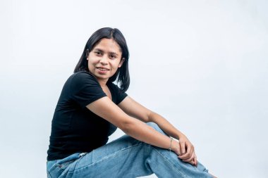 Siyah tişörtlü ve yırtık kotlu gülümseyen Endonezyalı kadın baş aşağı yerde oturuyor. Sıkıntı kavramı, beklemek ve yorgun gençlik yaşam tarzı beyaz arka planda izole edilmiş..