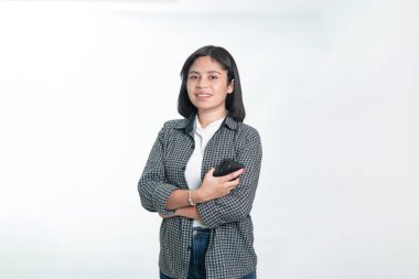 Kendine güvenen Endonezyalı bir kadın telefon tutarken kollarını kavuşturmuş poz veriyor. Mobil uygulama, teknoloji ve iş kavramları için temiz beyaz arkaplan.