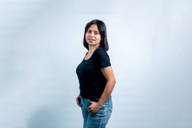 Endonezyalı genç bir kadının portresi beyaz arka planda, elleri belinde duruyor ve kameraya güvenle gülümsüyor..