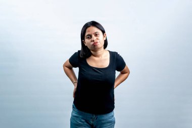 Beyaz bir arkaplan karşısında genç Endonezyalı bir kadının portresi, kameraya somurtkan bir ifadeyle bakıyor ve ellerini kalçasında, önde görüyor..