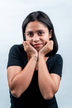 Beyaz arka planda genç bir Endonezyalı kadının portresi. Kameraya bakıyor, gülümsüyor ve iki eliyle çenesinde poz veriyor..
