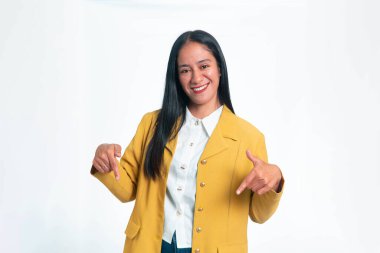 Sarı ceketli neşeli bir Endonezyalı kadın temiz beyaz bir arkaplana karşı iki eliyle boş fotokopi alanına doğru gülümsüyor ve işaret ediyor..