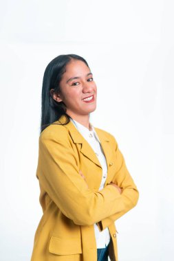 Sarı ceketli mutlu Endonezyalı bir kadının portresi kollarını kavuşturmuş beyaz bir stüdyonun arka planında kameraya bakıyor..