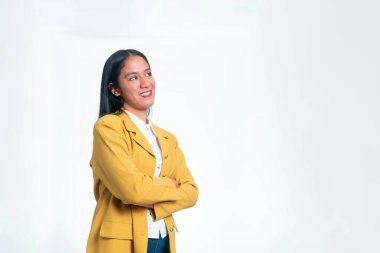 Sarı ceketli mutlu Endonezyalı bir kadının portresi kollarını kavuşturmuş, beyaz arka planda umut verici bir ifadeyle yukarı bakıyor..