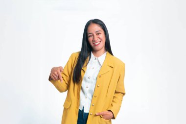 Sarı ceketli, beyaz tişörtlü, gülümseyen Endonezyalı kadın kameraya doğru işaret ediyor, beyaz arka planda izole edilmiş..