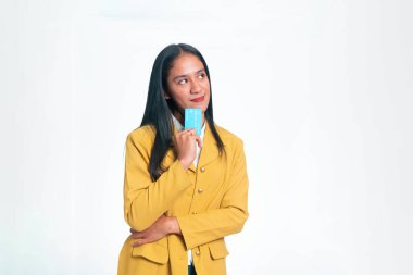 Gülümseyen Endonezyalı bir kadının portresi, beyaz arka planda izole edilmiş mavi bir kredi kartını tutarken düşünceli bir şekilde yüzünü çeviriyor..