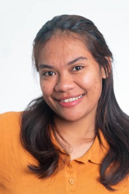 Uzun siyah saçlı, turuncu polo tişörtlü ve kameraya içten bir şekilde gülümseyen mutlu Endonezyalı bir kadının vesikalığı..