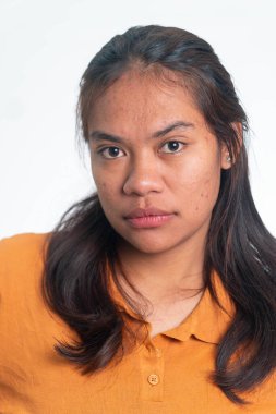 Tarafsız bir ifade ve sakin bir yüzle beyaz arka planda turuncu polo tişört giyen Endonezyalı genç bir kadının vesikalığı..