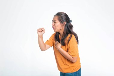 Turuncu gömlekli genç Endonezyalı kadın öksürüyor ve göğüs ağrısı çekiyor. Boğaz ağrısı, astım ya da mevsimsel virüs yüzünden acı çekiyor..