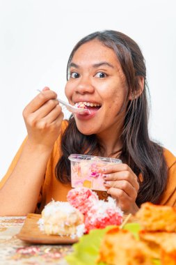 Endonezyalı kadın geleneksel atıştırmalıkların ve pembe içeceğin tadını çıkarıyor. Gıda ve yaşam tarzı içeriği için kopyalama alanı olan beyaz arkaplanda izole edilmiş.