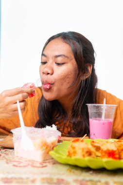 Endonezyalı kadın geleneksel atıştırmalıkların ve pembe içeceğin tadını çıkarıyor. Gıda ve yaşam tarzı içeriği için kopyalama alanı olan beyaz arkaplanda izole edilmiş.