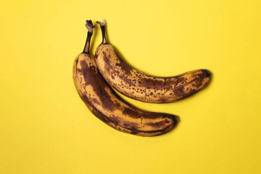 Sarı arka planda kahverengi benekli iki olgun muz. Gıda atığı, meyve depolama ve gıda bozulması kavramı.