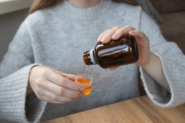 Kadın bir doz bardağını sıvı tıbbi şurupla dolduruyor. Grip tedavisi, ateş kontrolü, öksürük şurubu, alerji yönetimi.