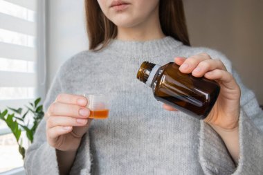 Sıvı tıbbi şurup ve ölçülü doz tutan bir kadın. Öksürük terapisi, grip önleyici, ateş düşürücü, alerji tedavisi.