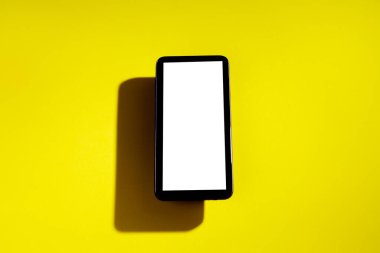 Sarı bir masanın üstünde beyaz ekranlı akıllı telefon. Cep telefonu konsepti. Beyaz ekran konsepti.