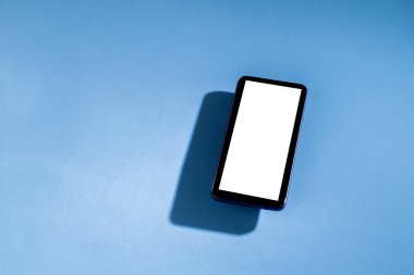 Mavi masanın üstünde beyaz ekranlı akıllı telefon. Cep telefonu konsepti. Beyaz ekran konsepti.