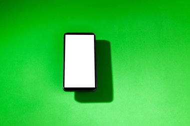 Yeşil masanın üstünde beyaz ekranlı cep telefonu. Akıllı telefon konsepti. Beyaz ekran konsepti.