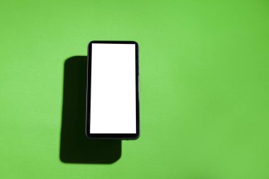Yeşil masanın üstünde beyaz ekranlı cep telefonu. Akıllı telefon konsepti. Beyaz ekran konsepti.