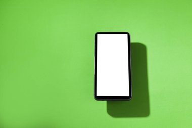 Yeşil masanın üstünde beyaz ekranlı cep telefonu. Akıllı telefon konsepti. Beyaz ekran konsepti.