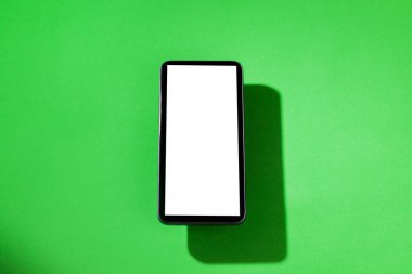 Yeşil masanın üstünde beyaz ekranlı cep telefonu. Akıllı telefon konsepti. Beyaz ekran konsepti.