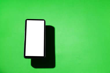 Yeşil masanın üstünde beyaz ekranlı cep telefonu. Akıllı telefon konsepti. Beyaz ekran konsepti.