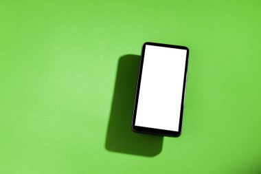 Yeşil masanın üstünde beyaz ekranlı cep telefonu. Akıllı telefon konsepti. Beyaz ekran konsepti.