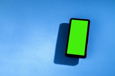 Mavi masadaki yeşil ekranlı cep telefonu. Akıllı telefon konsepti. Yeşil ekran konsepti.