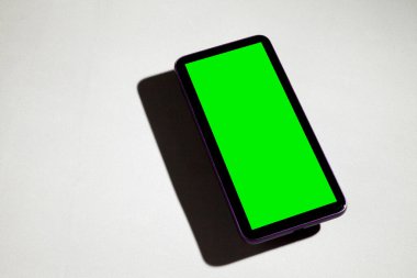 Gri masadaki yeşil ekranlı cep telefonu. Akıllı telefon konsepti. Yeşil ekran konsepti.