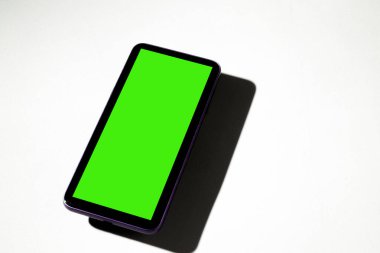 Gri masadaki yeşil ekranlı cep telefonu. Akıllı telefon konsepti. Yeşil ekran konsepti.