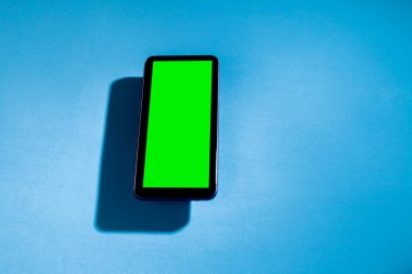 Mavi masadaki yeşil ekranlı cep telefonu. Akıllı telefon konsepti. Yeşil ekran konsepti.