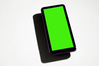 Gri masadaki yeşil ekranlı cep telefonu. Akıllı telefon konsepti. Yeşil ekran konsepti.