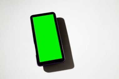 Gri masadaki yeşil ekranlı cep telefonu. Akıllı telefon konsepti. Yeşil ekran konsepti.