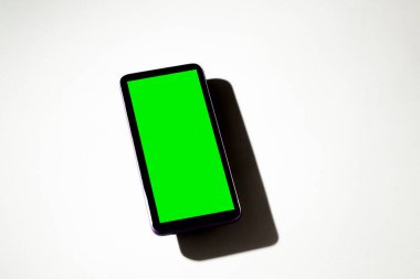 Gri masadaki yeşil ekranlı cep telefonu. Akıllı telefon konsepti. Yeşil ekran konsepti.