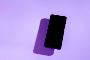 Mor bir masanın üstünde siyah ekranlı akıllı telefon. Cep telefonu konsepti. Mor konsept.