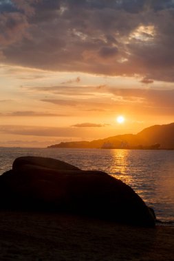 Ilhabela sahilindeki kayaların arasında altın gün batımı. Paradisiacal ve tropik Brezilya plajı. Taş konsepti. Altın günbatımı konsepti.