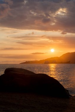 Ilhabela sahilindeki kayaların arasında altın gün batımı. Paradisiacal ve tropik Brezilya plajı. Taş konsepti. Altın günbatımı konsepti.