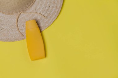 Sarı arka planda hasır şapka ve güneş kremi ambalajı. Mesaj için yer var. Şapka konsepti. Sombrero kavramı.