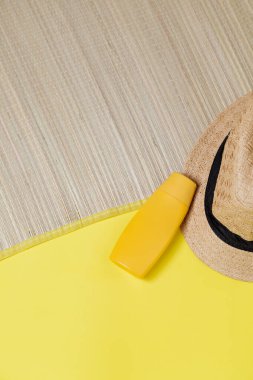 Sarı arka planda hasır şapka ve yüz nemlendirici ambalajı. Uzayı kopyala Yaz kavramı. Cilt bakımı kavramı.
