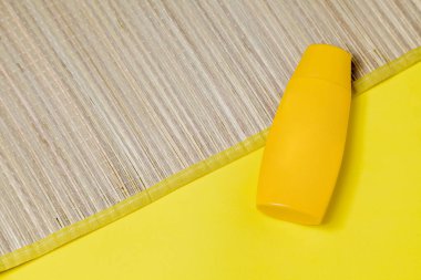 Sarı arka planda bir şişe güneş kremi ile saman hasırı. Yaz aksesuarları konsepti. Güzellik konsepti. Boşluğu kopyala.