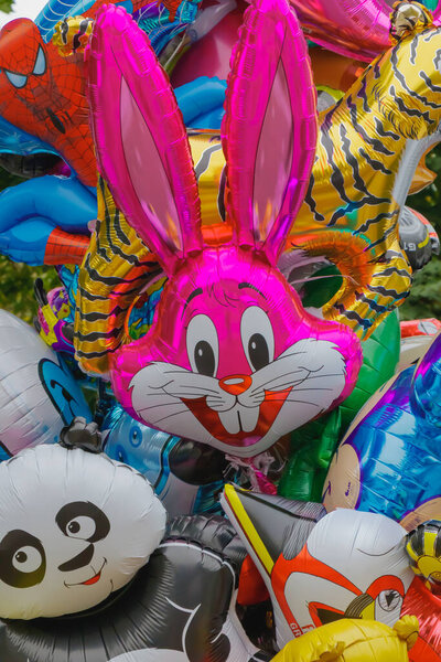 Ярко окрашенные гелиевые воздушные шары в форме мультяшных животных и персонажей, включая розового кролика, панду и тигра, выставленные на открытом воздухе на торжество или в семейном парке.