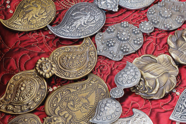 Коллекция металлических украшений ручной работы с детальными узорами и культурными мотивами, выполненная на богатой красной вышивке. Изображение подчеркивает безумное мастерство и традиционное искусство.