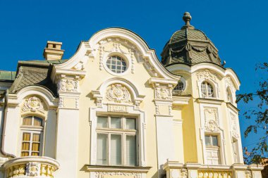 Karmaşık barok detayları, kubbeli çatısı ve zarif sarı-beyaz cephesi olan güzel korunmuş tarihi bir bina berrak mavi bir gökyüzünün altında, zamansız Avrupa mimarisi sergilenmektedir..