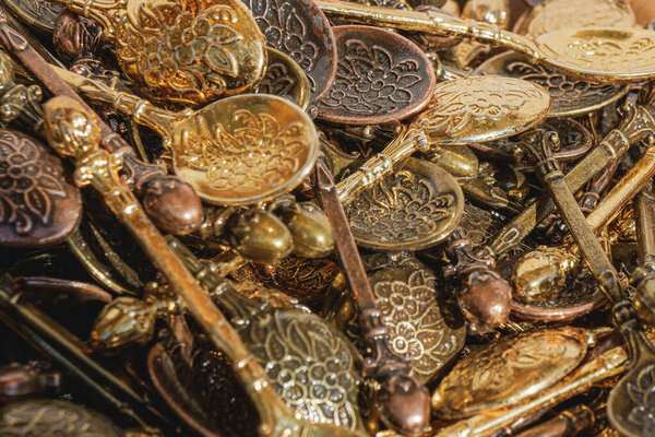 Коллекция металлических ложек ручной работы в золотом, бронзовом и медном цветах, выставленных на рынке. Замысловатые цветочные гравюры и металлические отражения подчеркивают мастерство ремесла.