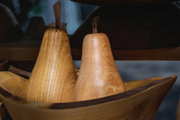 Two handcrafted wooden pears with smooth texture and visible wood grain displayed in a rustic bowl at an artisan market. The soft lighting enhances the natural tones and craftsmanship.