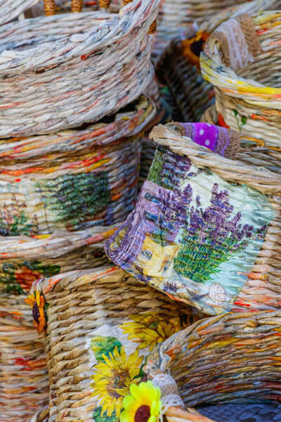 Decorative woven baskets featuring sunflower and lavender patterns are stacked at a local market. The natural textures and vivid colors highlight creativity, craftsmanship, and rustic artistry.